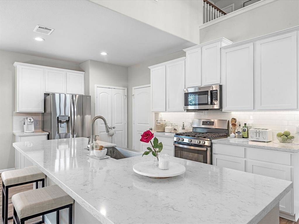 This modern kitchen features sleek white cabinetry, stainless steel appliances, and a spacious marble countertop island with seating. Bright and inviting, it offers ample storage and a contemporary feel.