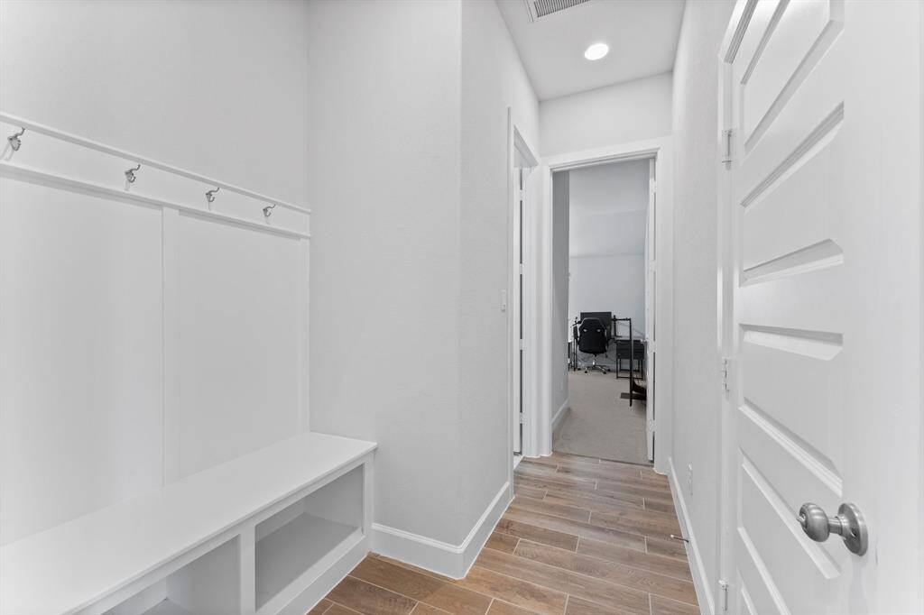 This is a neat, well-lit mudroom with built-in storage, including a bench and coat hooks, with tiled flooring and a view into another room.