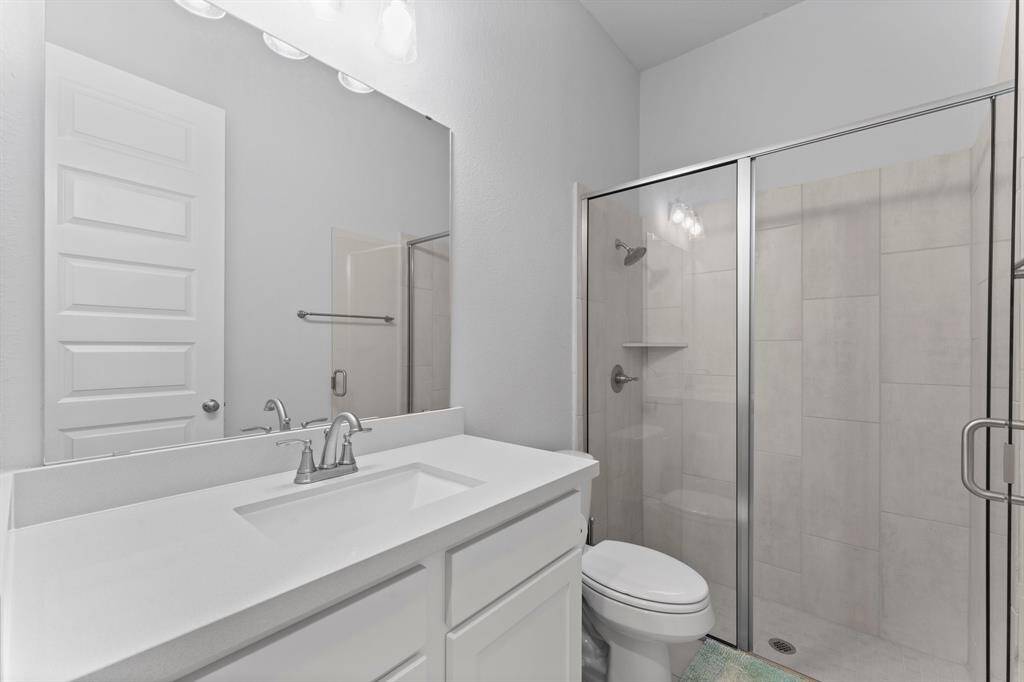 This is a modern, clean bathroom featuring  a single sink vanity with ample counter space,  and a walk-in shower with glass doors.