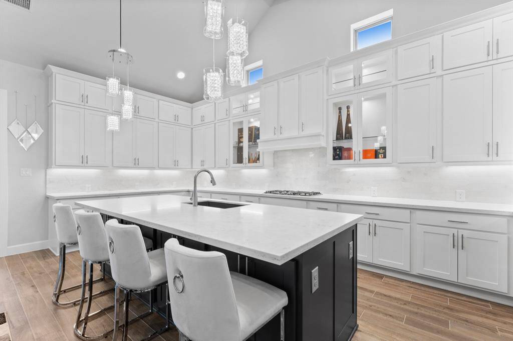 This modern kitchen features white cabinetry, a contrasting dark island with seating, elegant pendant lights,