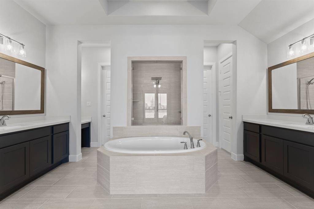 This spacious bathroom features a modern design with dual vanities, a large soaking tub, and a separate shower. Neutral tones and elegant fixtures complete the look.