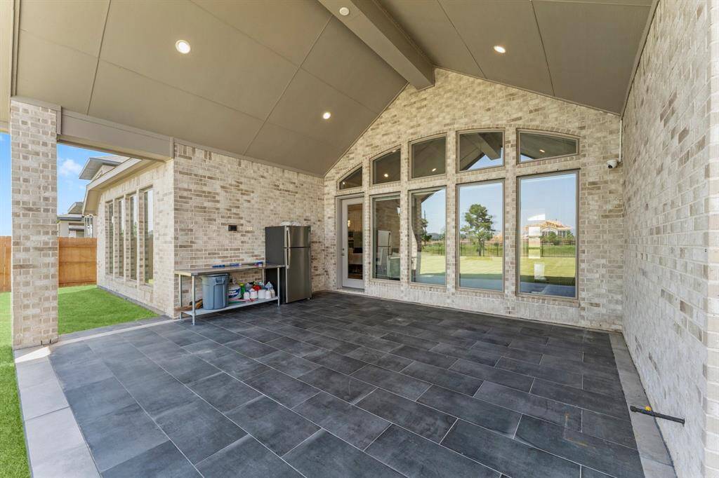 covered patio with slate tile flooring and large windows, offering a view of the backyard and beyond. The area is complemented by a high ceiling with recessed lighting, plenty space to build  an outdoor  kitchen.