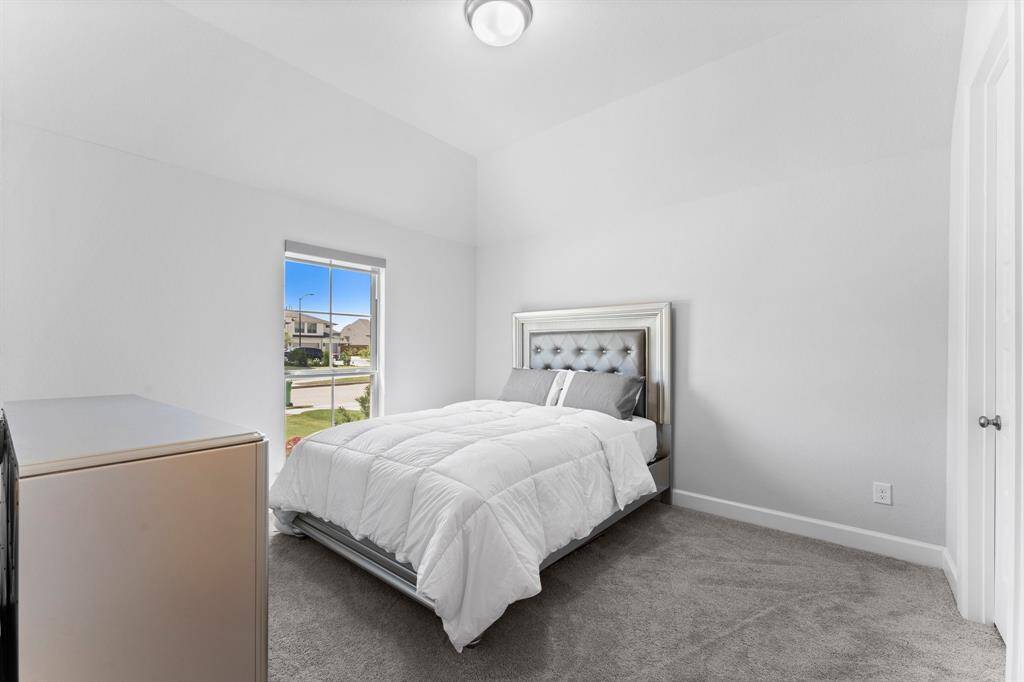 This is a bright, cozy bedroom featuring carpeted flooring, a large window with a street view, ready simple space with potential for personalization.