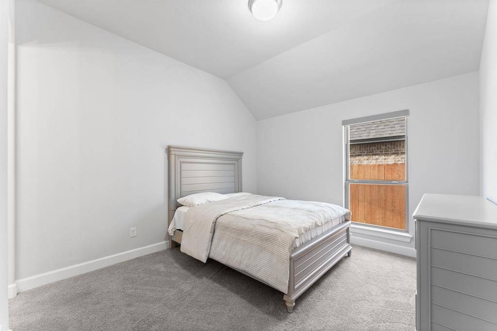 Bedroom featuring a sloped ceiling, plush carpeting, a large window for natural light, and neutral color tones.