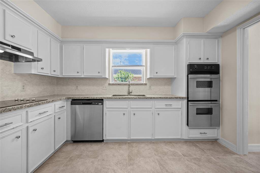 Updated kitchen with granite countertops, white cabinetry, stainless steel appliances and a large window above the sink.