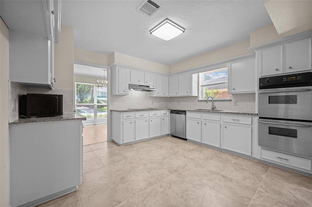 Updated kitchen with granite countertops, white cabinetry, stainless steel appliances, and a large window above the sink.
