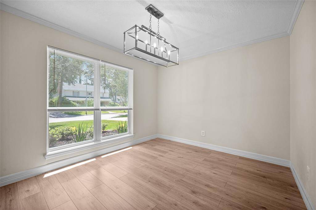 Bright dining room with laminate flooring, large front-facing window and a modern rectangular chandelier.