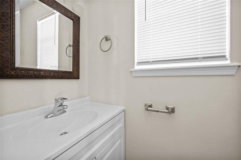 Half-bath with vanity, decorative framed mirror and window with blinds for natural light.