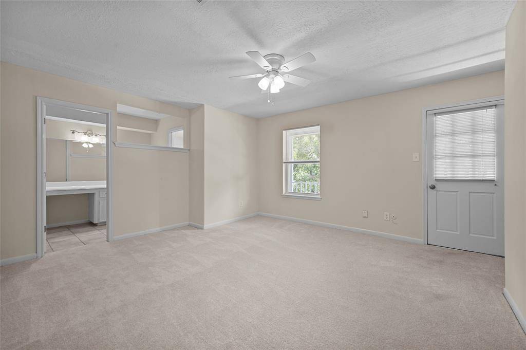 Spacious carpeted primary bedroom with ceiling fan, private balcony access and en suite bathroom