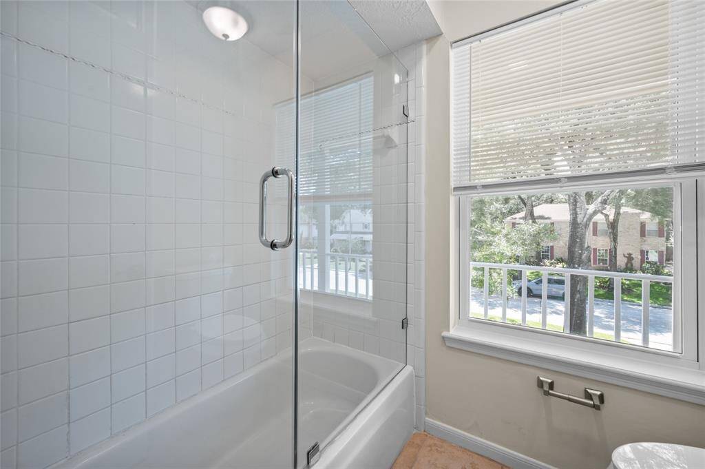 Bathroom with tiled shower/tub combo with frameless glass door and lots of natural light