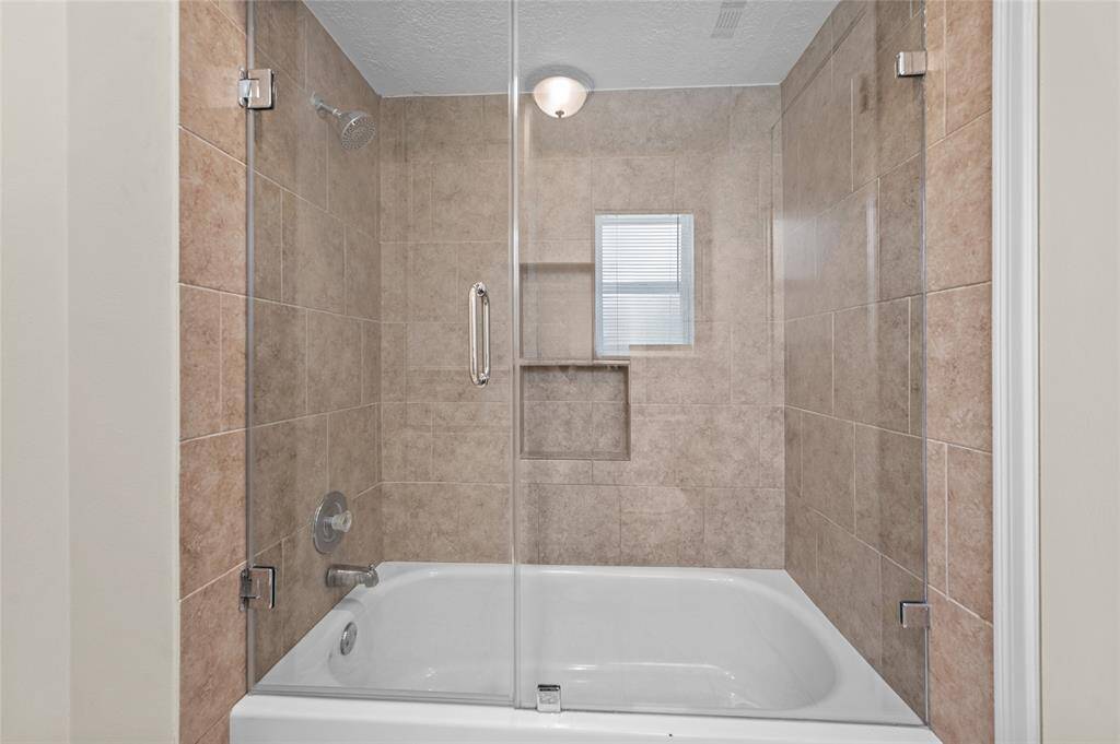 Guest bathroom with a tiled shower/tub combo, frameless glass door, and built-in shelving.