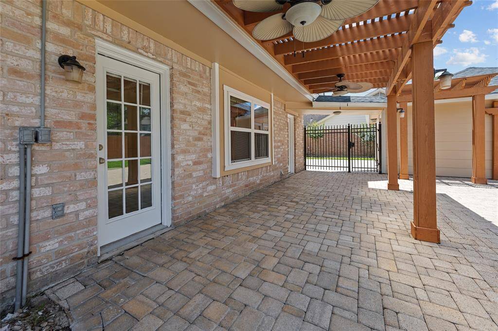 Covered patio with brick pavers, ceiling fans, and gated access to the driveway.