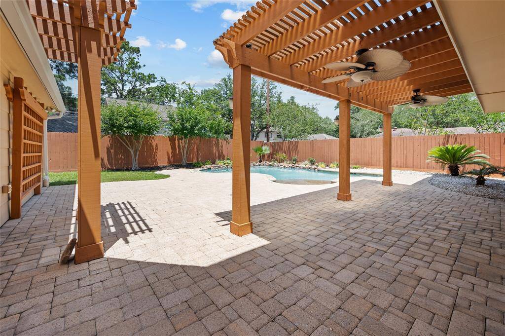 Spacious backyard with a pergola-covered patio, ceiling fans, and a view of the pool and landscaped yard.