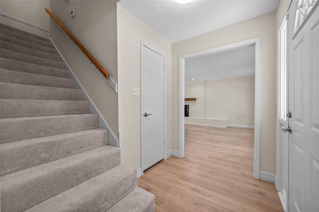 Inviting entryway features soft neutral tones, light vinyl flooring and a cozy carpeted staircase with a wooden handrail.