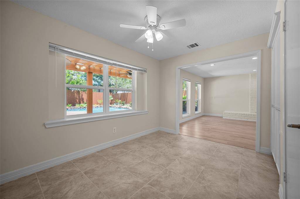 Bright dining area with tile floors, ceiling fan and large windows offering a clear view of the backyard and pool.