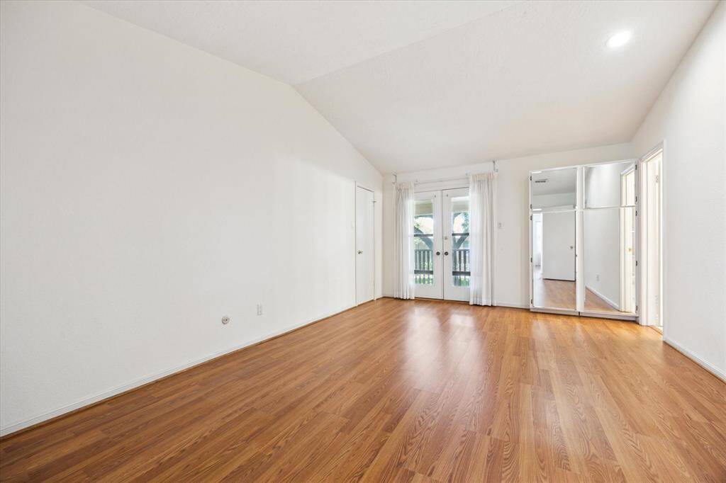 This spacious Primary room features hardwood floors, high ceilings, and ample natural light from French doors leading to a balcony. A mirrored closet adds functionality and style.