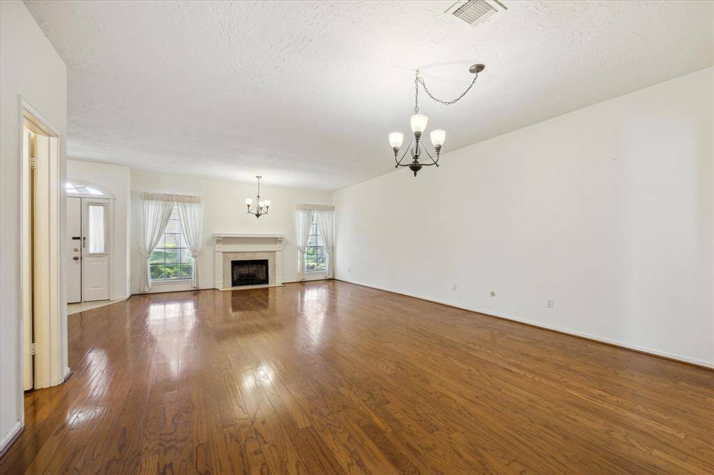 Spacious living area featuring hardwood floors, elegant light fixtures, and an open layout. Includes a staircase leading to an upper level and access to adjacent rooms. Ideal for entertaining and family gatherings.