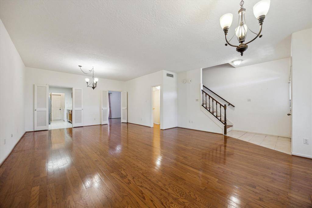 This spacious living room features hardwood floors, a cozy fireplace, large windows for natural light, and elegant chandeliers, creating a warm and inviting atmosphere.