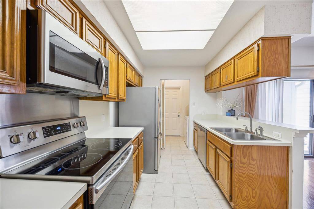 This kitchen features stainless steel appliances, wooden cabinetry, and a double sink. It has a clean, bright design with tiled flooring and ample counter space.