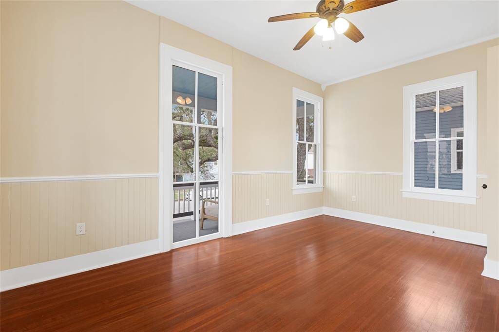 Unit 1: Wall-to-wall windows and warmth. This front bedroom is filled with soft natural light from three large windows and features warm hardwood floors, beadboard trim, and peaceful views of the tree-lined street.