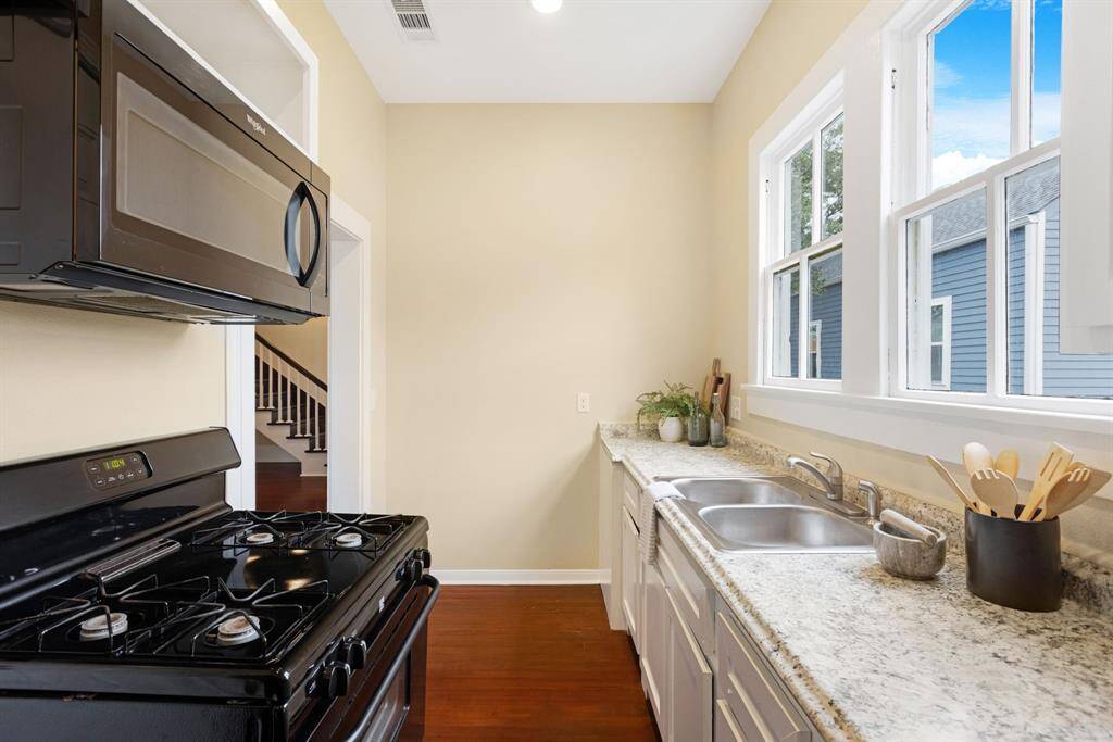 Unit 1: Simply charming. This galley-style kitchen combines efficiency with elegance—featuring granite-look formica countertops, crisp white cabinetry, black appliances, and a window that fills the space with soft, natural light.