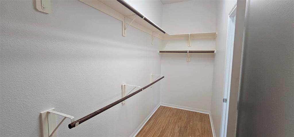 Spacious walk-in closet with multiple shelves and hanging rods, featuring laminate flooring and neutral walls, offering ample storage and organization options.