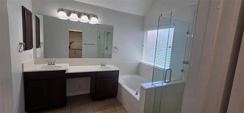 This bathroom features a double vanity with dark wood cabinets and a large mirror. It includes a glass-enclosed shower and a separate soaking bathtub, providing a bright and spacious feel with natural light from the window.