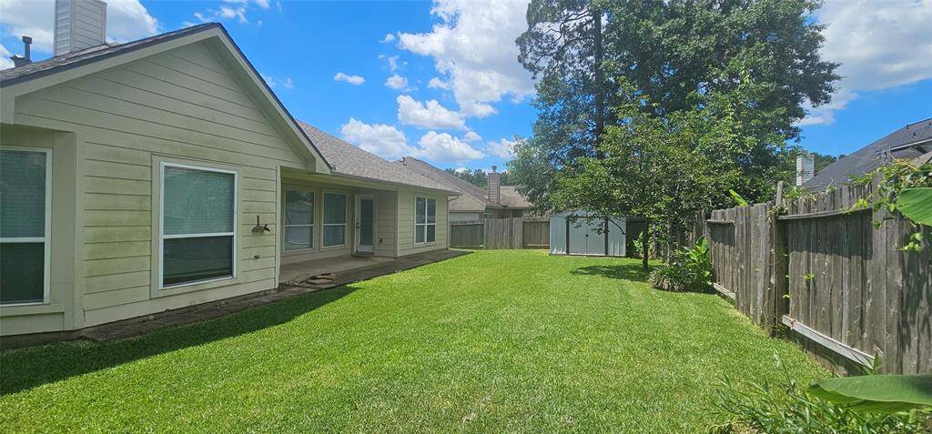 a spacious backyard with well-maintained green grass, a wooden fence, and a small storage shed. Perfect for outdoor activities and gardening.