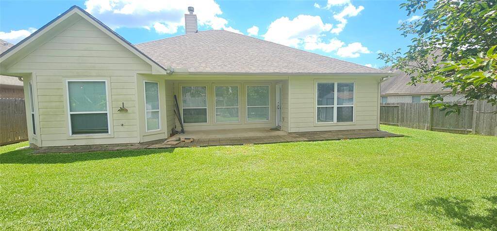 The house features a covered patio area with several large windows, allowing for plenty of natural light. It's enclosed by a wooden fence, offering privacy and a cozy outdoor space.