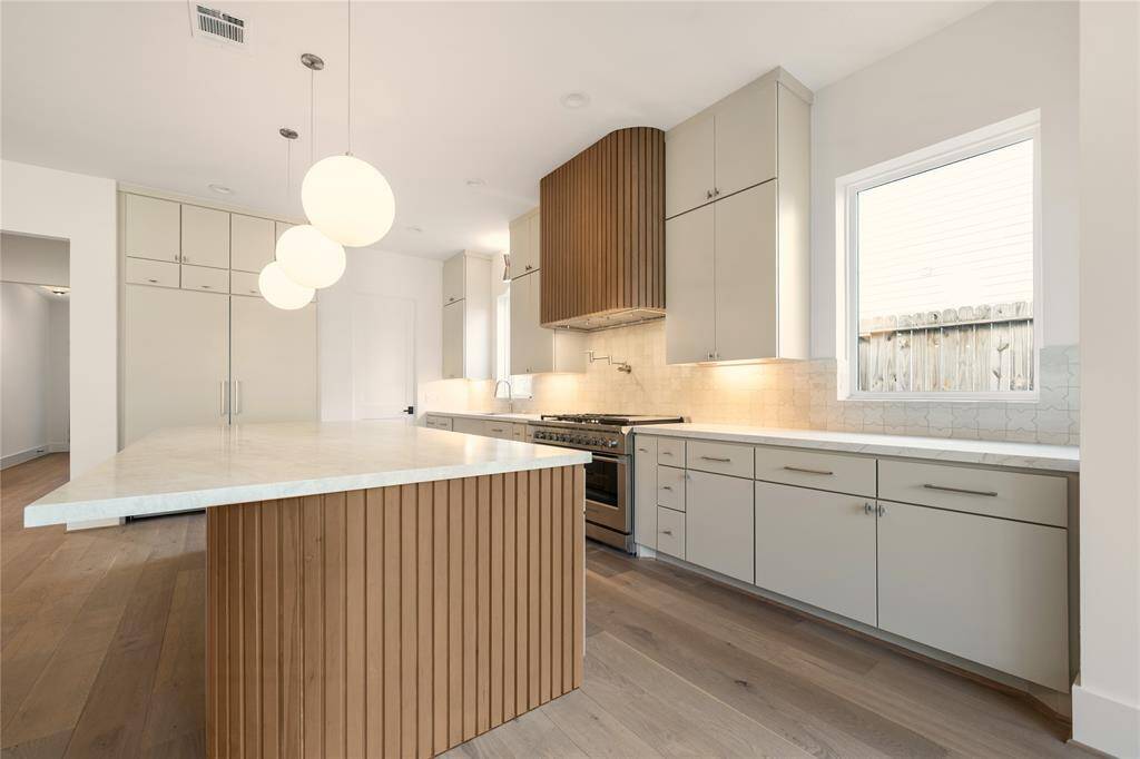Fisher & Paykel appliance package included in this home along with Taj Mahal quartz on the island and a pot filler above the stove. Pantry door is visible directly off the kitchen.