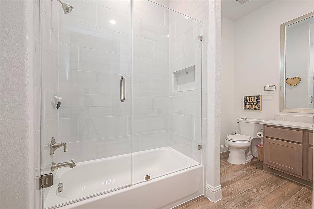 This modern bathroom features a sleek glass-enclosed shower with a tiled interior, a spacious vanity with storage, and wood-look flooring, creating a stylish and functional space.