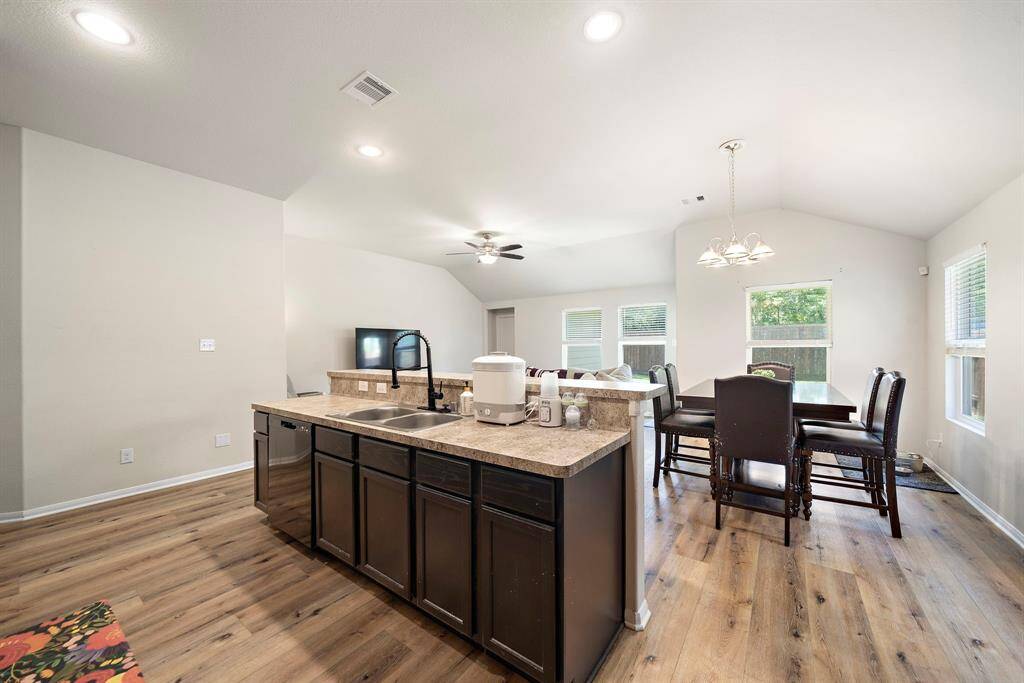 A spacious open-concept living area featuring a modern kitchen with a large island and dark cabinets, adjacent to a dining area with ample natural light from multiple windows.