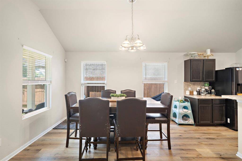 The space is open and airy with multiple windows, premium flooring, and dark cabinetry in the adjacent kitchen area.