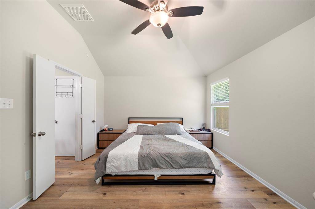 This bedroom features a vaulted ceiling with a modern ceiling fan, high-end flooring, and neutral walls. It includes a large window for natural light and a spacious walk-in closet.