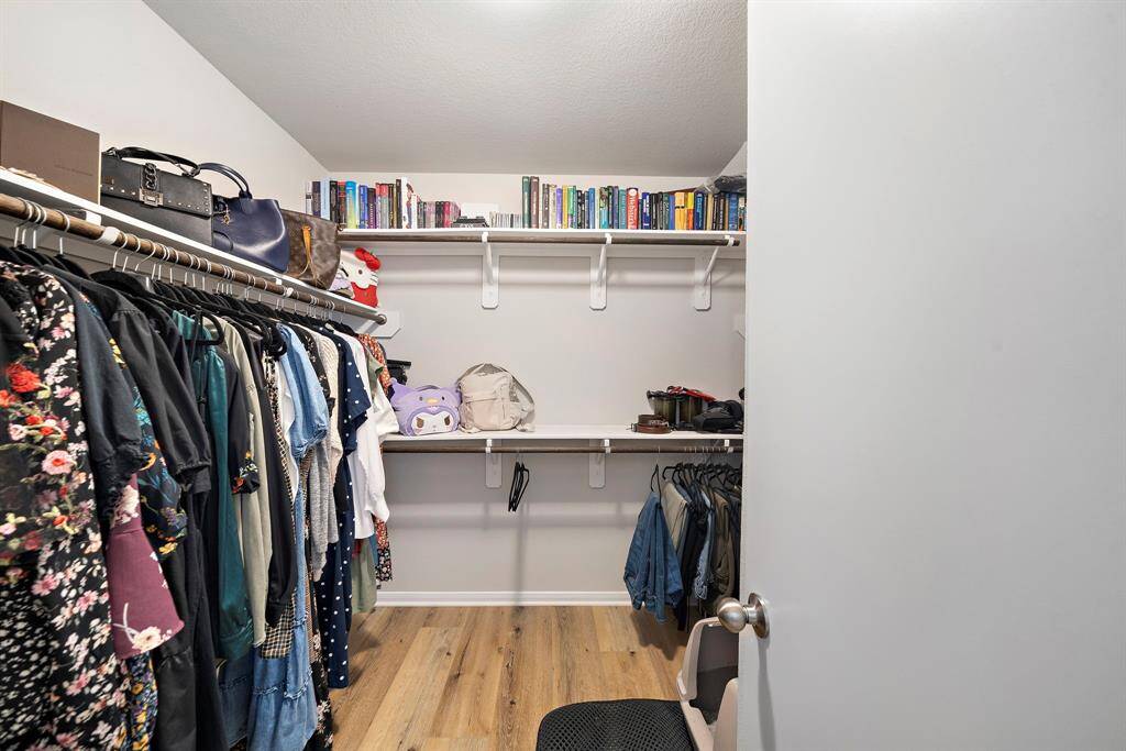 This photo shows a spacious walk-in closet with organized shelving, hanging rods, and storage space. It features wooden flooring and ample room for clothing and accessories, making it ideal for keeping everything tidy and accessible.