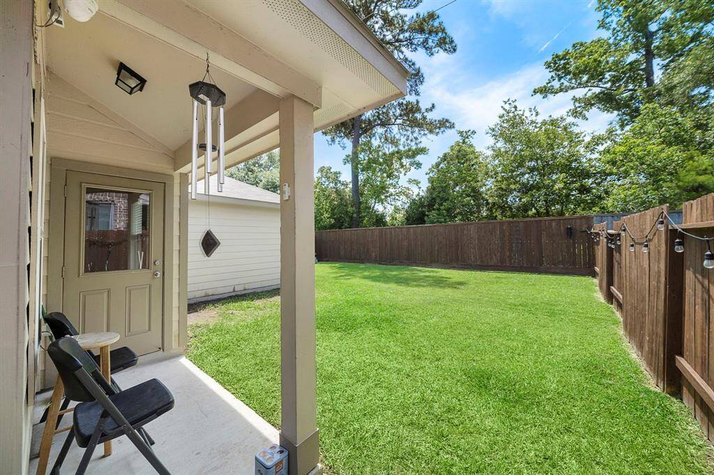 No Back Neighbor. This backyard features a cozy covered patio with seating and wind chimes, a spacious green lawn, and a wooden privacy fence adorned with string lights, perfect for outdoor relaxation and entertaining.