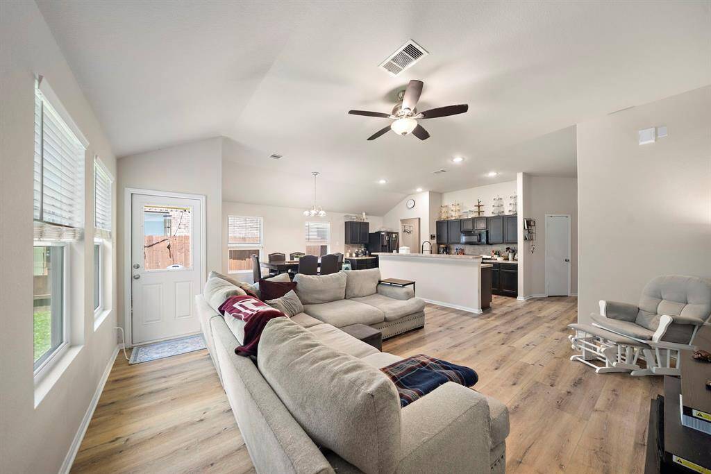 It features a comfortable seating arrangement, a ceiling fan, and ample natural light. The kitchen, with sleek cabinetry and an island, opens to the dining area, creating a seamless flow for entertaining.