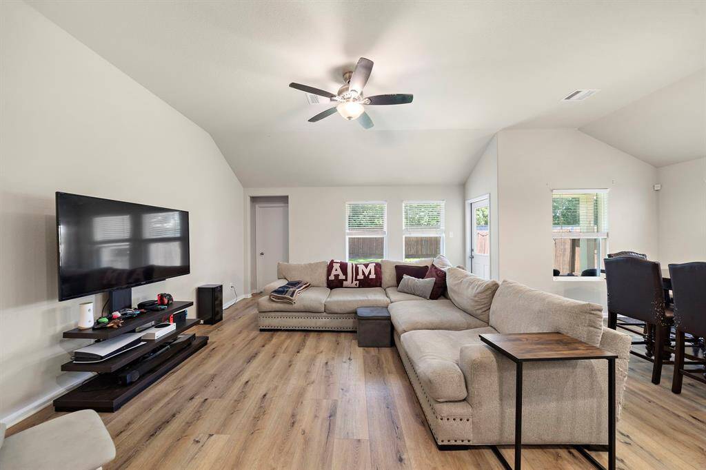 Bright and spacious living room with modern high-end vinyl flooring, a ceiling fan, and ample natural light from multiple windows. Perfect for entertaining.