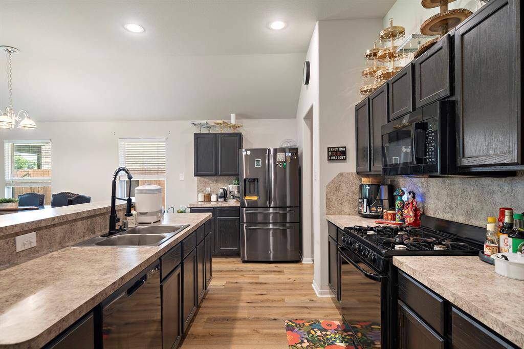 This kitchen features modern appliances, dark cabinetry, and an open layout with a breakfast bar. It has ample counter space, a gas stove, and natural light from two windows, creating a welcoming cooking area.
