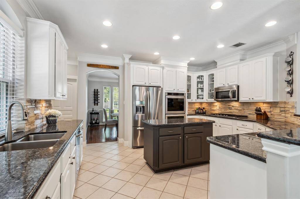 Kitchen features island with cookbook shelf, granite countertops, stone backsplash, under cabinet lighting and glass front corner cabinets.