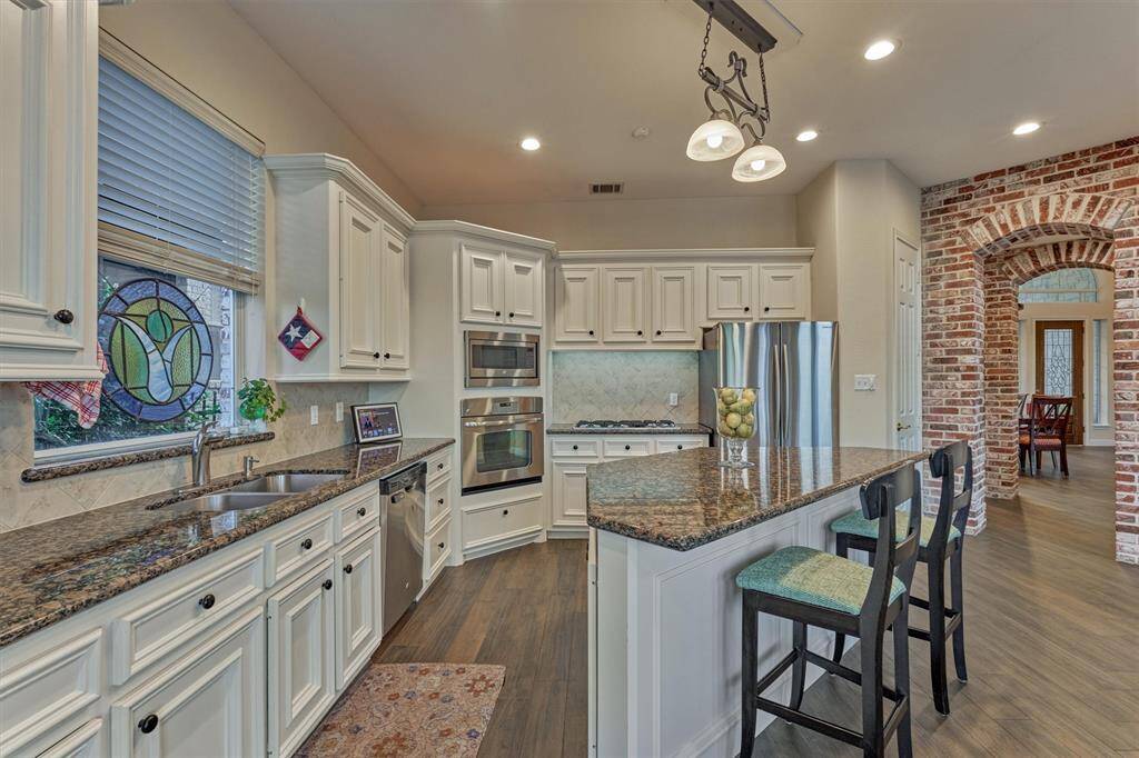 The center island offers additional seating. The kitchen is equipped with stainless steel appliances, including a five-burner gas cooktop, built-in microwave, dishwasher, and gas oven.