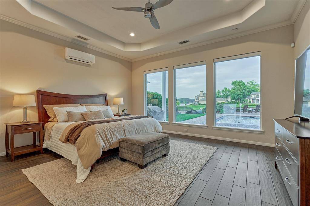The primary bedroom showcases an elegant tray ceiling and large, seamless windows overlooking the pool and lake.