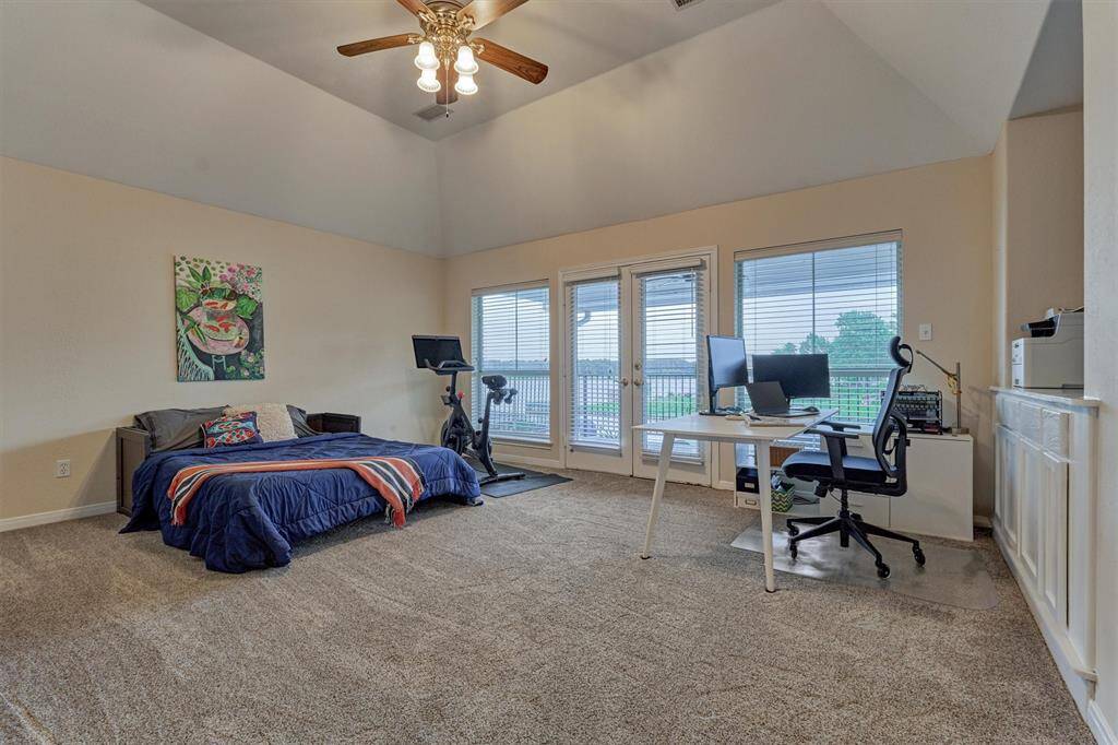 The game room, currently set up as a bedroom, features a high ceiling, built-in cabinetry and double doors leading to the balcony overlooking the lake.
