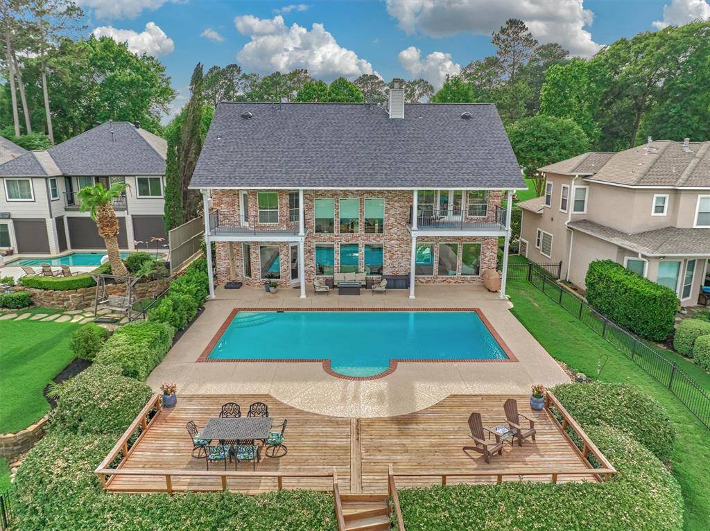 A closer look at the pool area reveals expansive decking with ample space for lounging and entertaining. The covered back porch spans the entire length of the home, providing shade and comfort, while two separate balconies on the second floor offer elevated views of the lake and backyard.