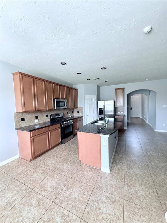 This spacious kitchen features modern appliances, granite countertops, and ample wood cabinetry. It includes a central island with a sink, tile flooring, and a bright, open layout connecting to the adjacent living areas.