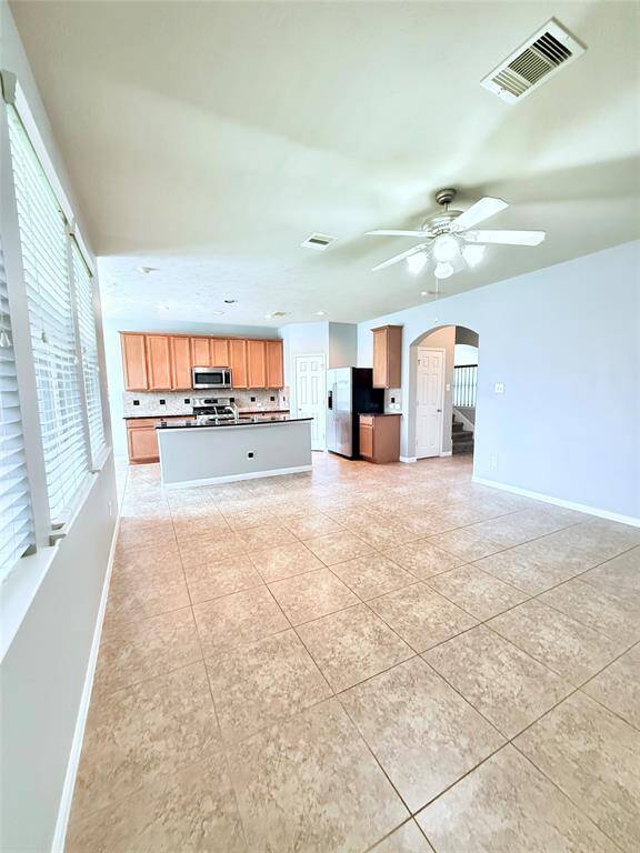The kitchen features wooden cabinets, a central island, and a ceiling fan for added comfort.