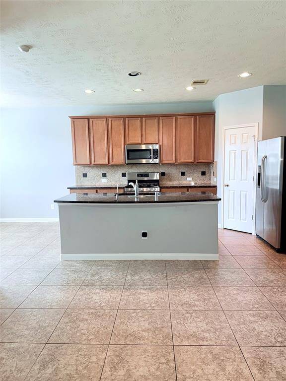 Modern kitchen with tiled flooring, granite countertops, and wooden cabinetry. Includes stainless steel appliances, a central island with a sink, and recessed lighting. Bright and spacious layout.