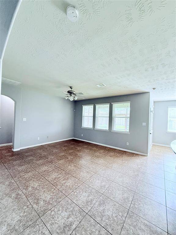 Spacious living room with abundant natural light, featuring elegant tiled flooring and a ceiling fan for comfort.