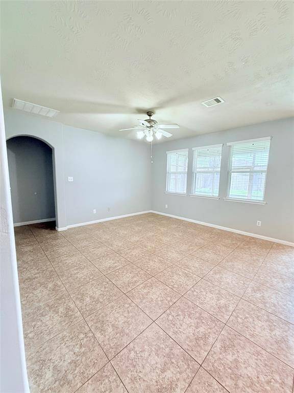 Bright and spacious living room featuring elegant tile flooring, a ceiling fan, and abundant natural light from large windows. Perfect for relaxing or entertaining.