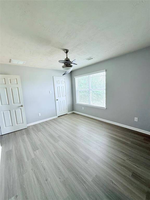 Bright and spacious second bedroom featuring sleek flooring, a ceiling fan, and ample natural light from large windows.